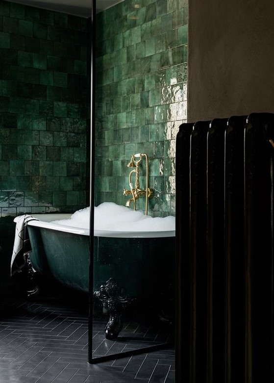 an exquisite dark green clawfoot bathtub surrounded with glossy green tiles on the walls