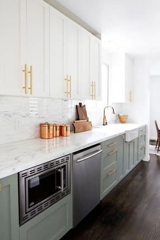 an exquisite two tone kitchen with white and sage green cabinets, a white quartz backsplash and countertops plus touches of gold