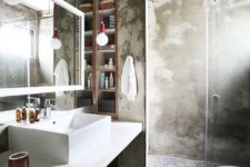 an industrial bathroom done of concrete, with a white floating vanity, red bulbs, a large lit up mirror
