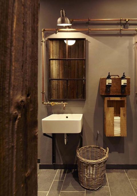 an industrial bathroom with concrete walls, a basket, exposed piping and reclaimed wood here and there