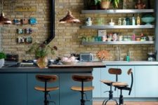 an industrial kitchen with sleek blue cabinets, metal countertops, a brick wall, extended piping and copper lamps