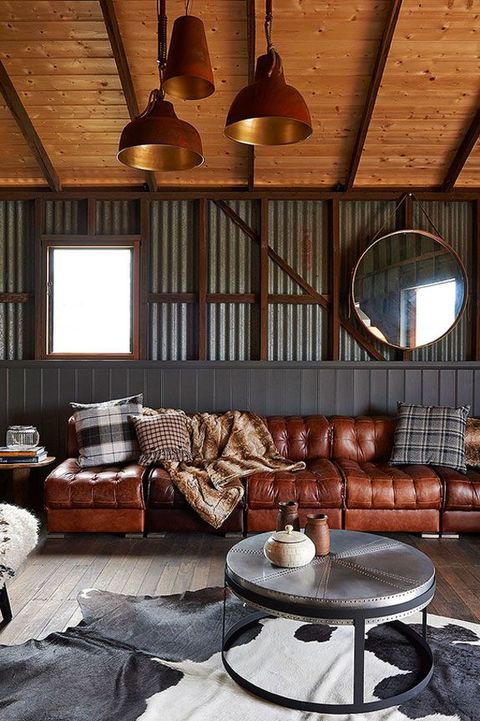 an industrial space with corrugated steel walls, a wooden ceiling, metal lamps and a table, an animal rug and a leather sofa