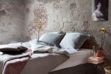 an industrial space with shabby chic brick walls, a grey upholstered bed, a refined artwork and a metal nightstand