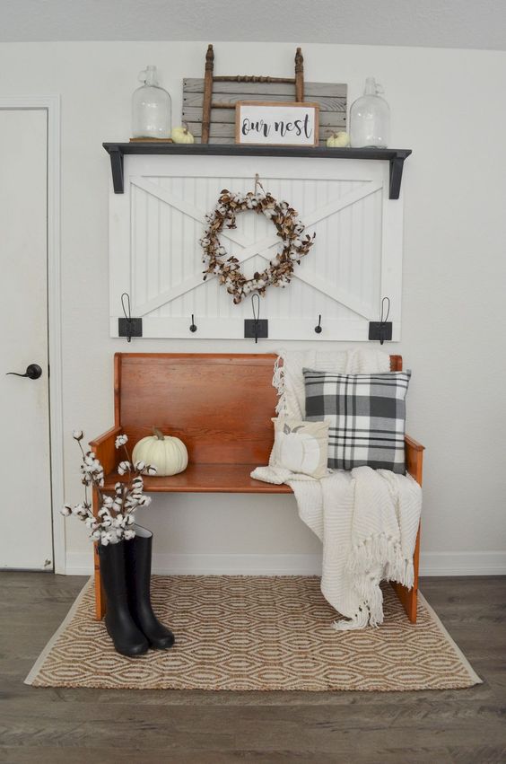 an inviting farmhouse entryway with an amber stained wooden bench, a wooden rack, some decor and artworks