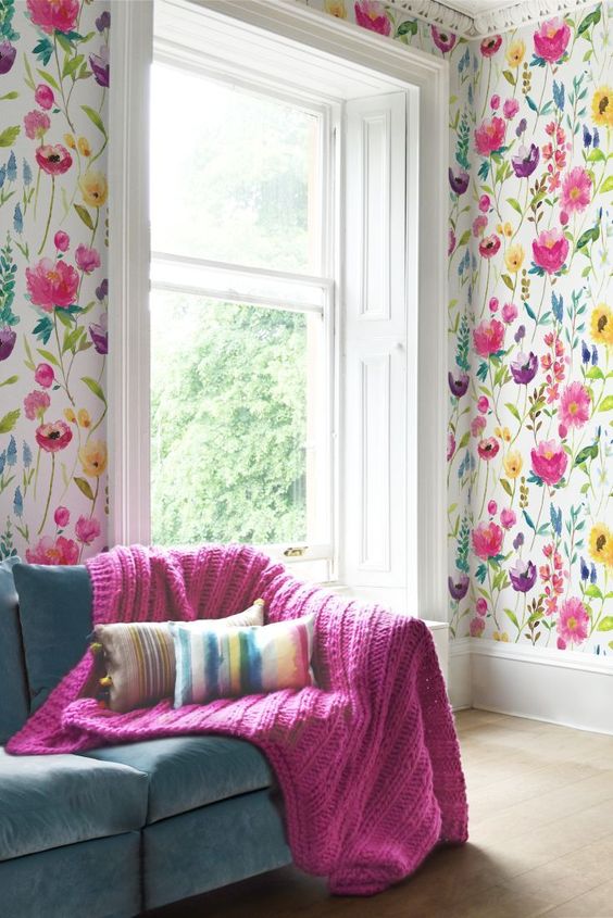 a bright and bold living room with bold floral wallpaper walls and a matching hot pink blanket