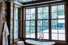 a beautiful and simple chalet bathroom clad with rich-stained weathered wood, with a metal tub and much light through windows