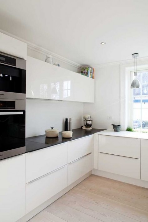a black and white minimalist kitchen with sleek and shiny cabinets, pendant lamps and built in appliances