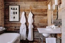 a chalet bathroom clad with reclaimed wood, with a brick wall, a tub, a free-standing sink and vintage lamps