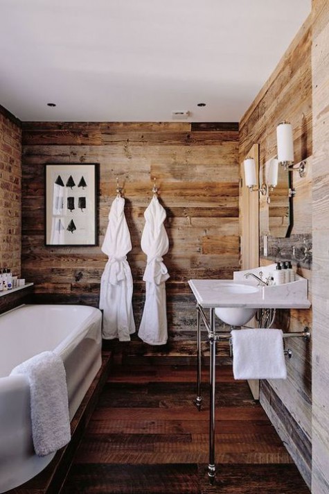 a chalet bathroom clad with reclaimed wood, with a brick wall, a tub, a free-standing sink and vintage lamps
