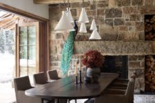 a chalet dining room with dark vintage furniture, a stone clad fireplace, pendant lamps and doors that are opened