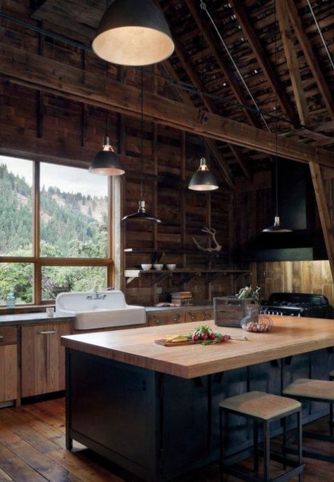 a chalet kitchen clad with reclaimed wood, with a alrge black kitchen island, vintage metal lamps and a large window
