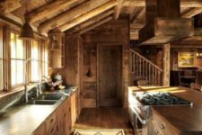a chalet kitchen fully clad with wood, with wooden beams, weathered wood cabinets, a boho rug and porcelain pendant lamps