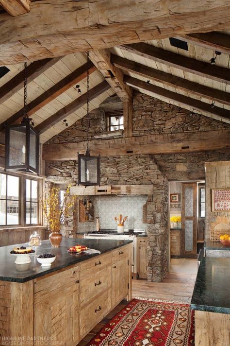 a chalet kitchen with a stone clad wall, wooden cabinets and a kitchen island, pendant lamps and skylights is very cozy