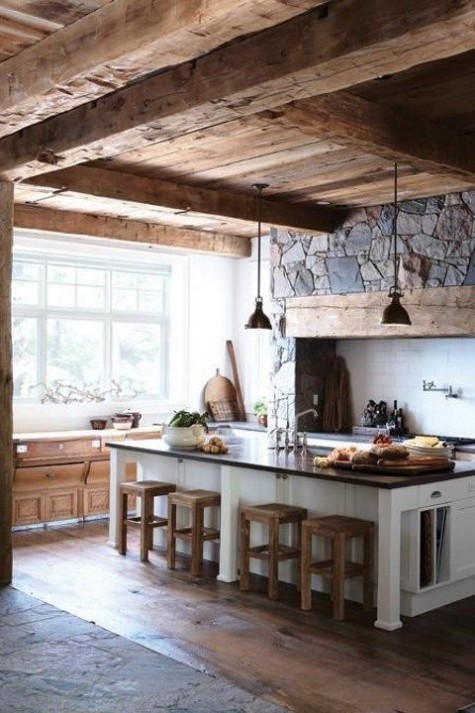 a chic chalet kitchen with a stone wall with built-in appliances, a large kitchen island, metal pendant lamps and a large window