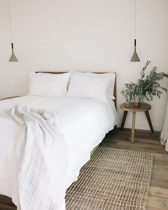 a chic minimalist bedroom with a wooden bed, stool nightstands, pendant lamps and a jute rug