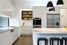 a chic minimalist kitchen in white, with sleek cabinets, marble countertops and black pendant lamps and stools