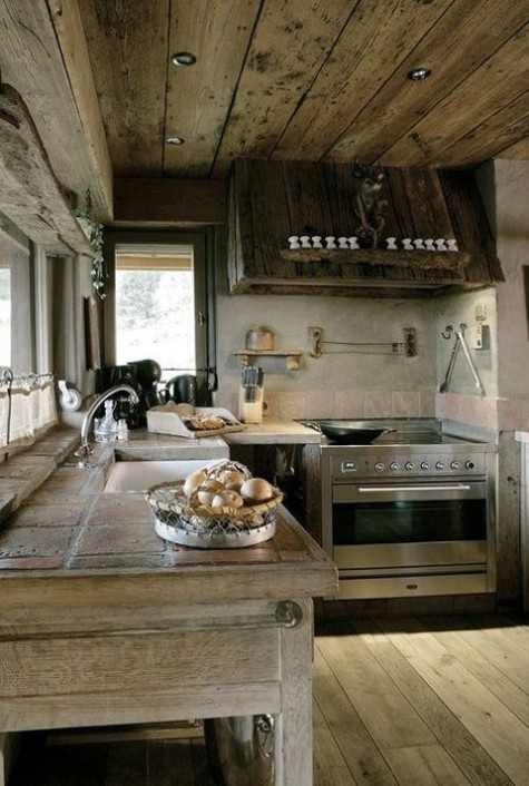 a chic modern chalet kitchen with reclaimed wood cabinets, tile countertops, a wooden ceiling and hood plus built-in lights