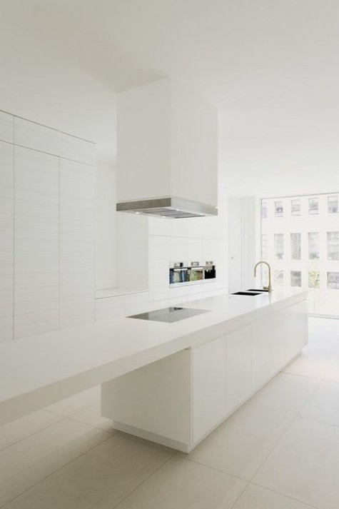 a chic white kitchen with sleek cabinets, a large hood and a long kitchen island that becomes a dining table at one end