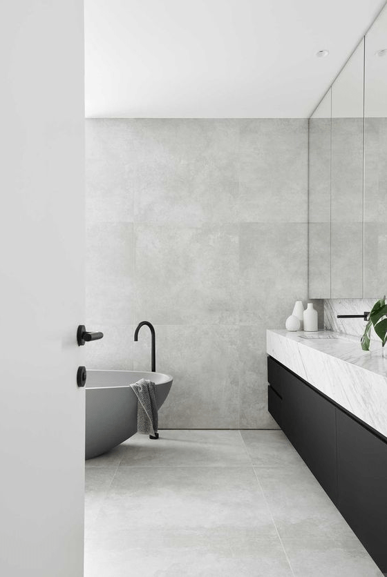 a clean minimal bathroom clad with grey stone, a black floating vanity with a stone countertop, a mirror cabinet and a concrete tub
