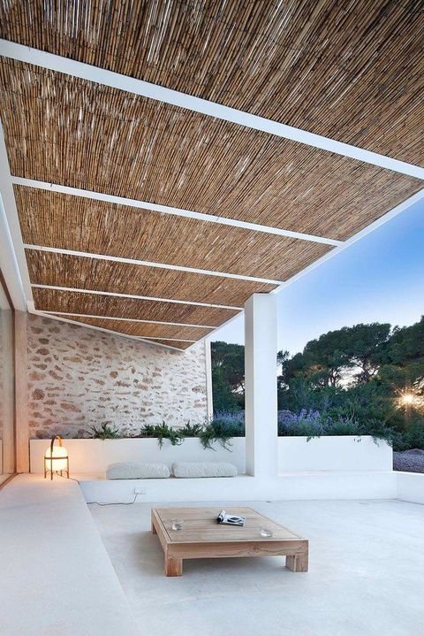 a clear minimalist terrace with a white concrete bench all along the space, a wooden table, some cushions and a lantern