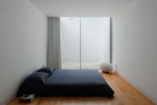 a cool minimalist bedroom with a large bed with black bedding, a catchy soft egg stool and a large window