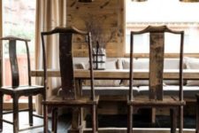 a cozy chalet dining space with wooden walls, an arrangement of black lamps, vintage furniture, a stone floor, a faux fur ottoman