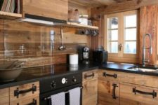 a cozy modern chalet kitchen all clad with sleek wood, with a glass backsplash, black stone countertops and black touches