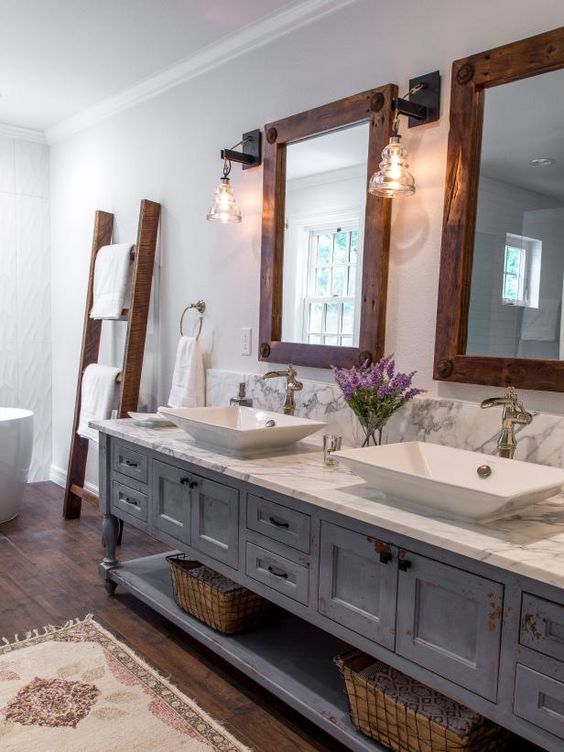 a farmhouse bathroom with a vintage blue vanity, wood frame mirrors, sconces, baskets and a ladder with towels