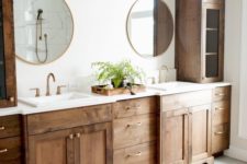 a farmhouse bathroom with dark stained furniture, round mirrors and chic sconces for a vintage feel