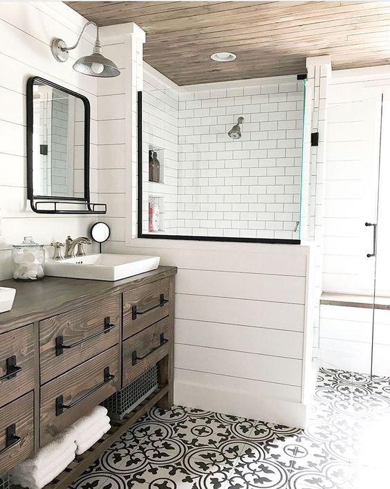 a farmhouse bathroom with white tiles and beadboard, printed tiles on the floor, a wooden vanity and vintage mirrors