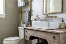 a farmhouse powder room with grey beadboard walls, a wooden vanity, a mirror in a wooden frame and vintage fixtures