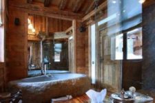 a gorgeous chalet bathroom clad with rich-stained wood, a stone tub, a shower space and a stone table