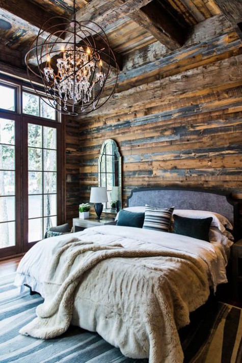 a gorgeous chalet bedroom clad with reclaimed wood, with a statement sphere and crystal chandelier and lots of faux leather and fur