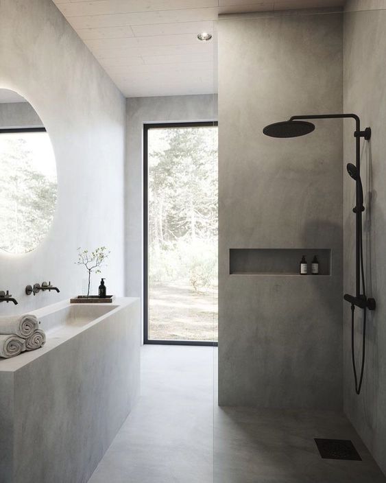 a grey minimalist bathroom clad with large scale tiles, black fixtures, a monolith vanity with a sink and a large window
