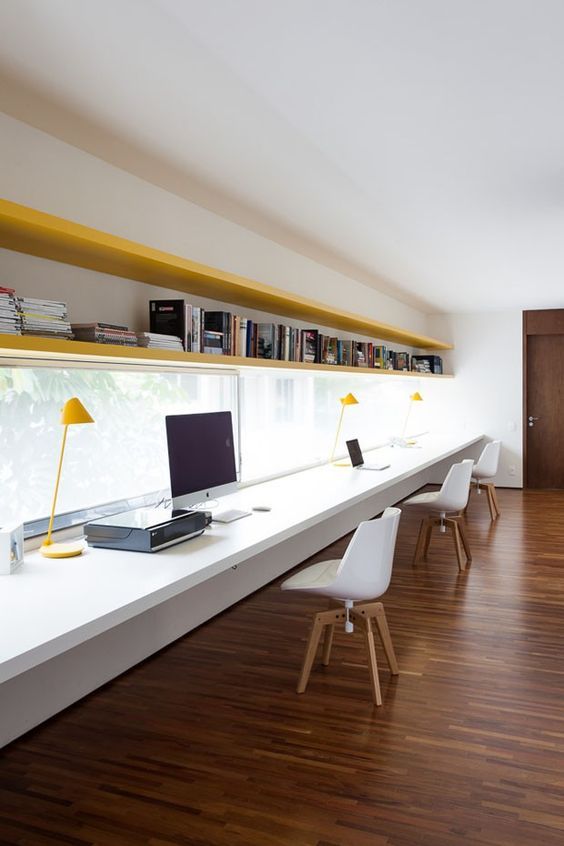 a large minimalist home office with bright yellow shelves, a long floating desk, white chairs and yellow lamps