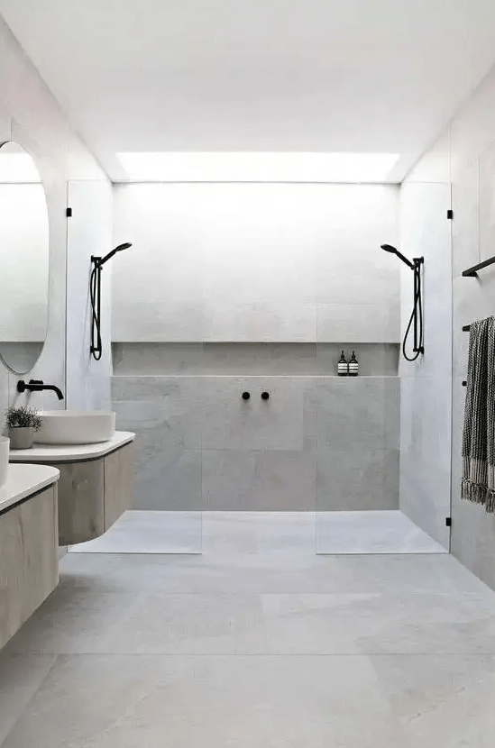 a minimalist bathroom clad with concrete, two floating vanities, round sinks, black fixtures and glass partitions