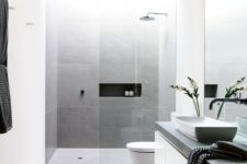 a minimalist bathroom clad with grey and white tiles, a floating vanity, a concrete countertop and a large mirror
