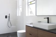a minimalist bathroom with white walls, dark tiles on the floor, a wooden vanity, catchy appliances and a mirror