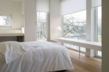 a minimalist bedroom with several windows, a sleek white vanity or desk, a smaller vanity on the left and a bed