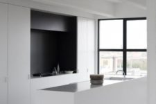a minimalist black and white kitchen with a matte backsplash and a black hood, a long kitchen island with a shiny countertop