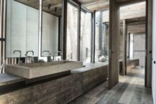 a minimalist chalet bathroom clad with dark weathered wood, with a stone sink, large windows and lamps