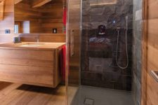 a minimalist chalet bathroom clad with light-colored wood, with a shower space done with stone tiles and built-in lights