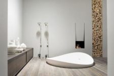 a minimalist chalet bathroom with white walls, a reclaimed wooden floor, a built-in tub, a fireplace and a firewood storage