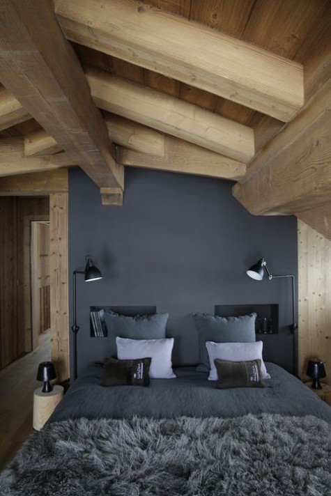 a minimalist chalet bedroom with a black statement wall, grey bedding, a faux fur bedspread and wooden beams