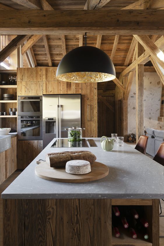 a minimalist chalet kitchen done with sleek wood, with a large kitchen island, a black lamp and a stone countertop