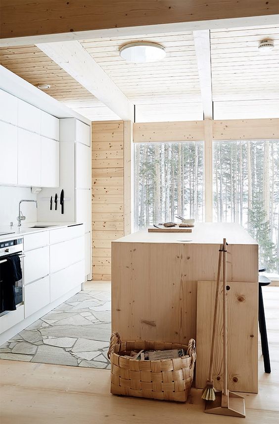 a minimalist chalet kitchen with a plywood kitchen island, sleke white cabinets and a stone floor flooded with natural light