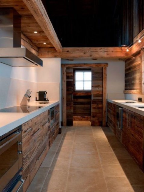 a minimalist chalet kitchen with wooden cabinets, white concrete countertops, metal appliances and a black ceiling
