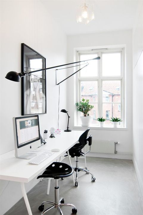 a minimalist double home office with a long desk, black chairs, an artwork and a long sconce