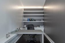 a minimalist home office with a grey accent wall, white furniture and open shelves plus built-in lights