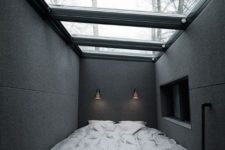 a minimalist masculine bedroom with dakr walls, a glazed ceiling and a bed plus sconces to look at the sky